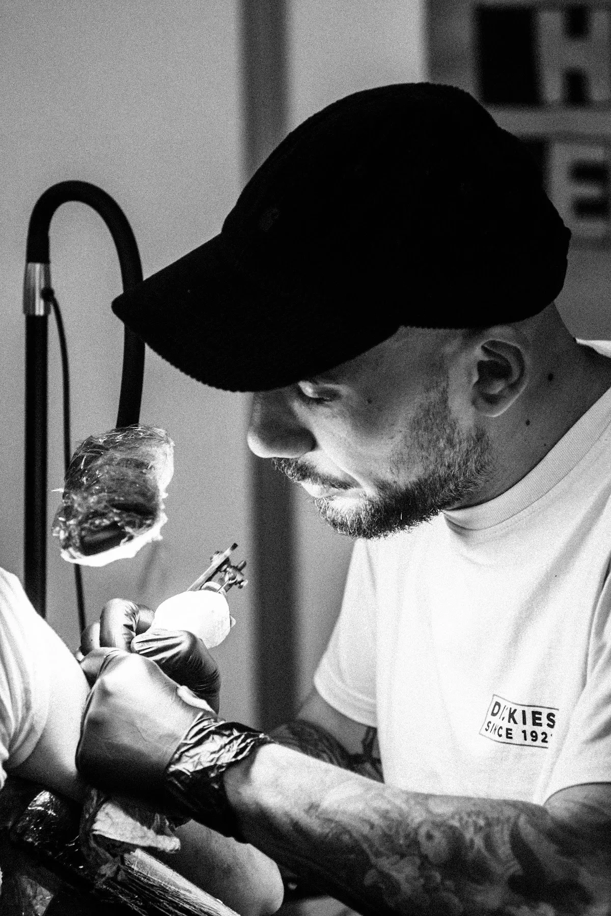 Ota au travail, penché sur un tatouage, casquette noire